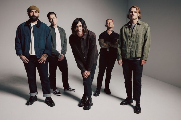 Band members of rock group Sleeping With Sirens posing together in dark jackets and casual wear against a plain grey backdrop.